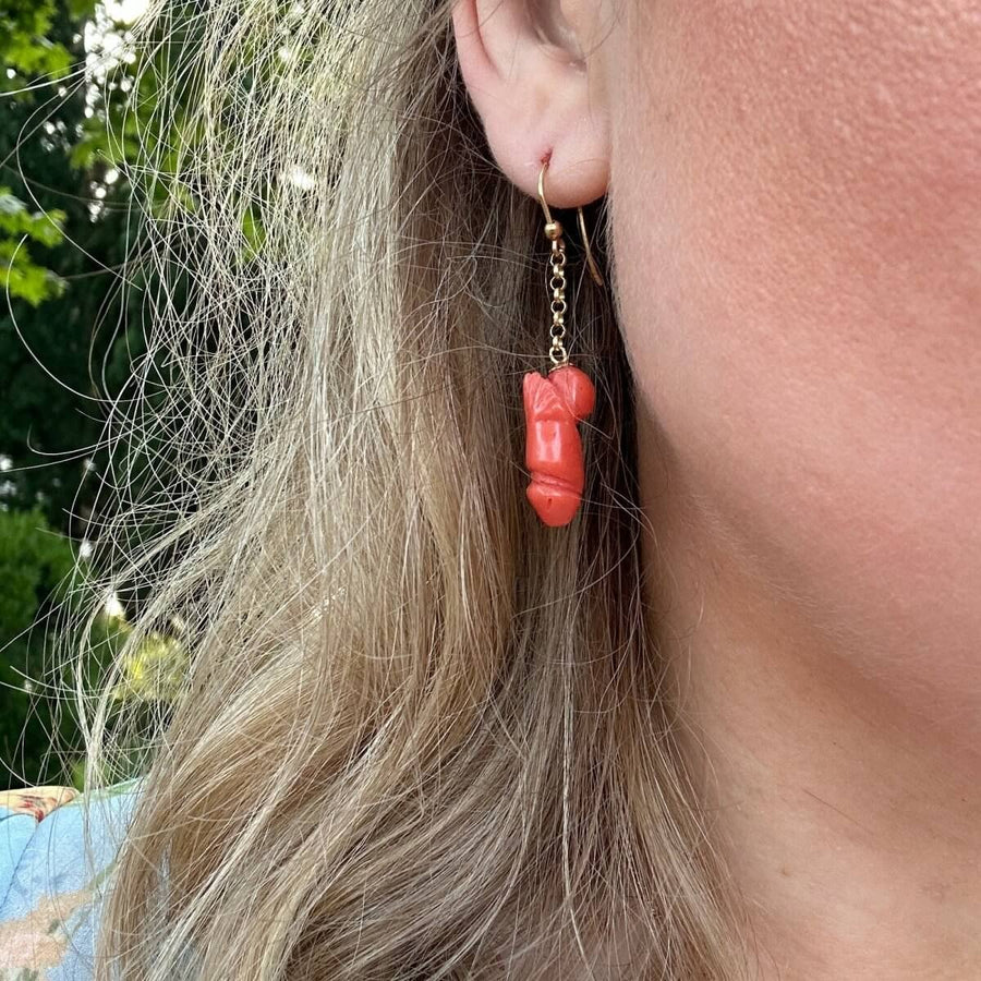 Vintage 18ct gold drop earring featuring a carved coral phallus against a blurred outdoor background.